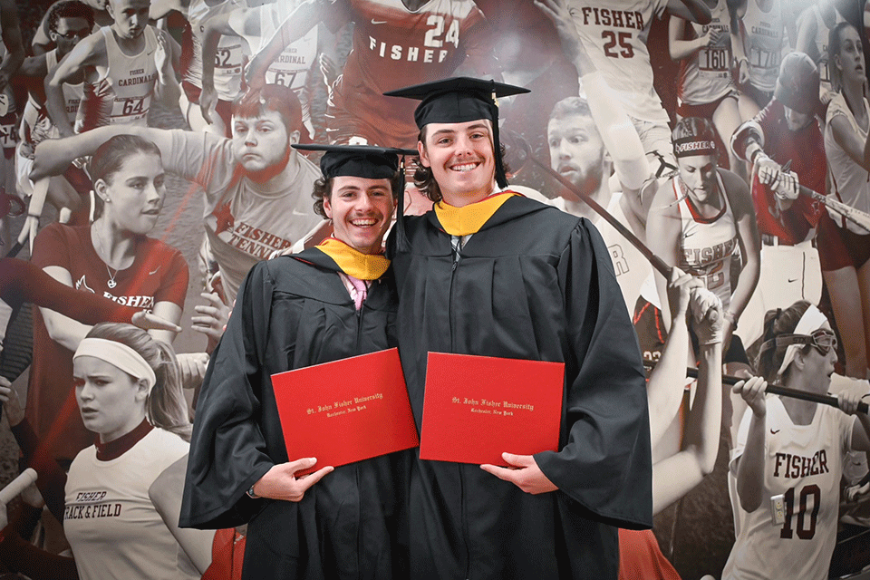 Two student-athletes pose with their diplomas.