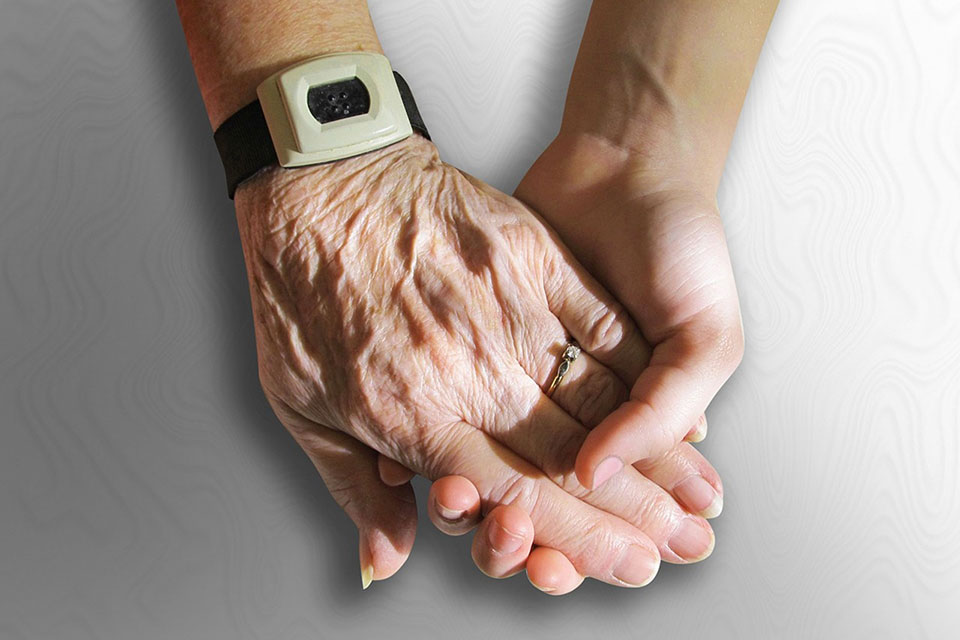 An elder person holds hands with a younger person.