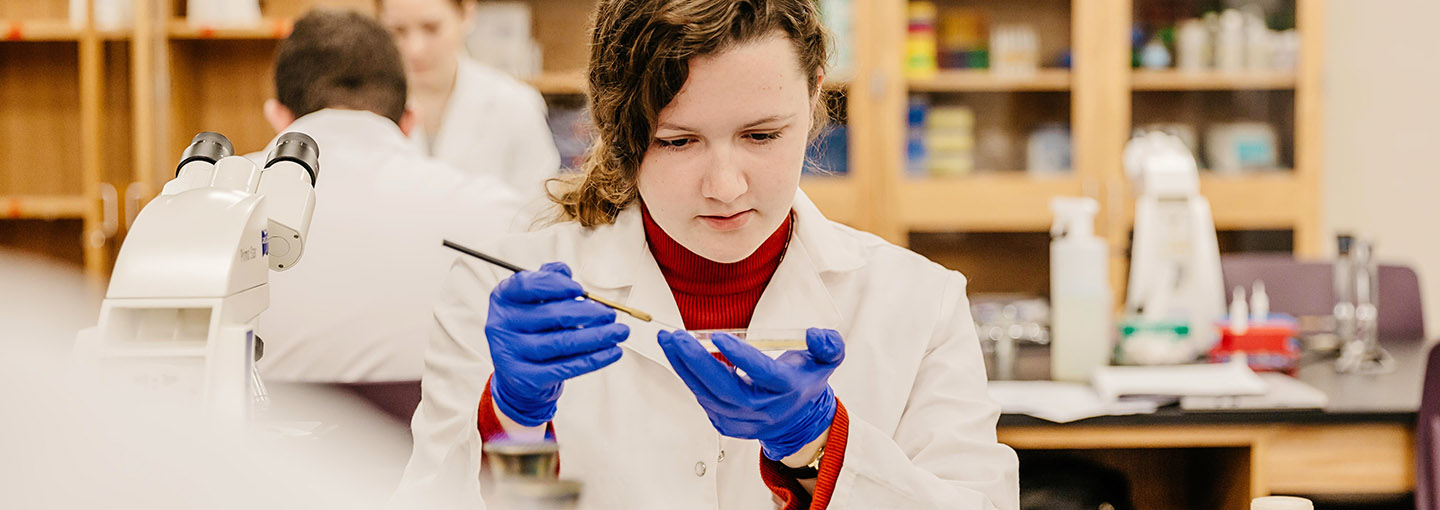 A student inspects a petri dish in a lab setting.
