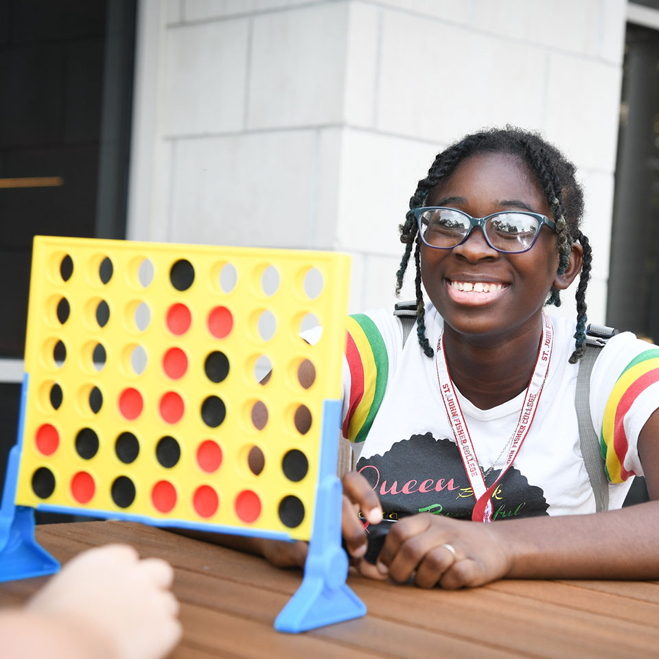 A student playing connect four with a friend outside.